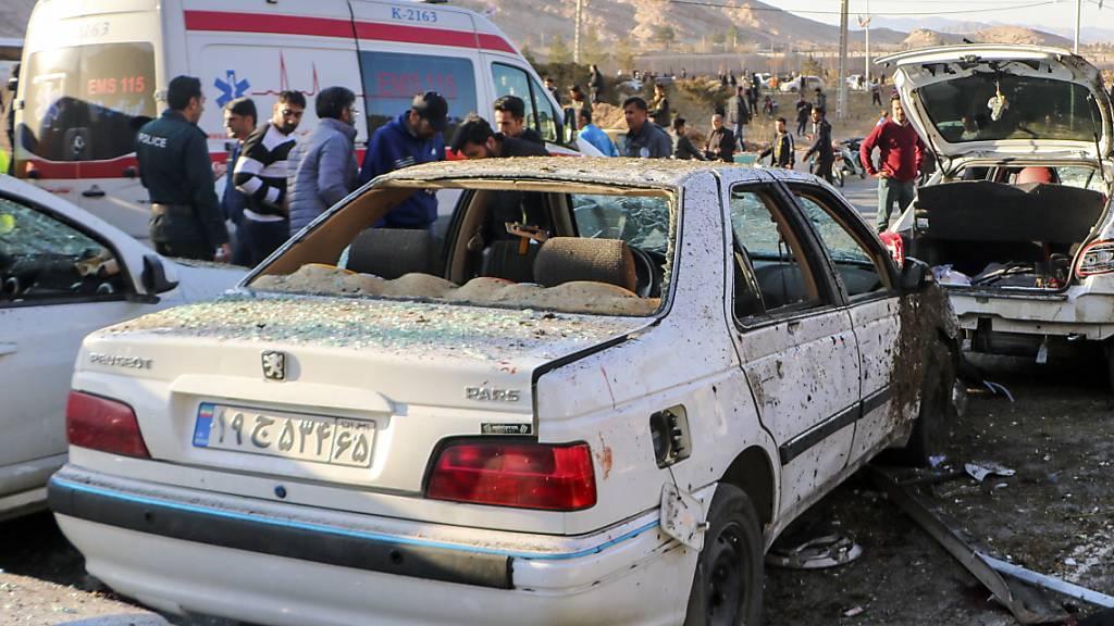 Menschen stehen neben zerstörten Autos nach einer Explosion. Am Todestag des mächtigen iranischen Generals Ghassem Soleimani sind in dessen Heimatstadt Kerman bei zwei Explosionen mehr als 100 Menschen in den Tod gerissen worden. Foto: Uncredited/Tasnim News Agency/AP/dpa - ACHTUNG: Nur zur redaktionellen Verwendung und nur mit vollständiger Nennung des vorstehenden Credits