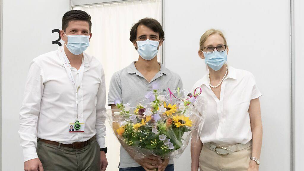 Pedro Ferreira (Mitte) ist der hundertausendste Einwohner mit einer Zweitpimpfung im Kanton Basel-Stadt und hat dafür einen Blumenstrauss erhalten.