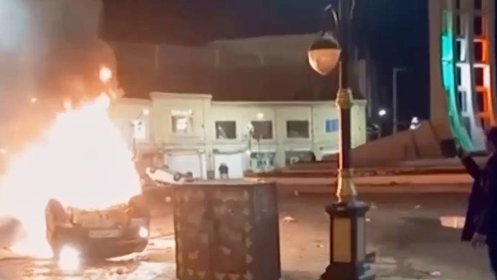 HANDOUT - Dieser Ausschnitt aus einem vom iranischen Staatsfernsehen via AP veröffentlichten Video zeigt einen Mann, der ein Gerät hält, um brennende Fahrzeuge während nächtlicher Massenproteste in Zandschan zu dokumentieren. Foto: Uncredited/Iran state TV/AP/dpa - ACHTUNG: Nur zur redaktionellen Verwendung im Zusammenhang mit der aktuellen Berichterstattung und nur mit vollständiger Nennung des vorstehenden Credits