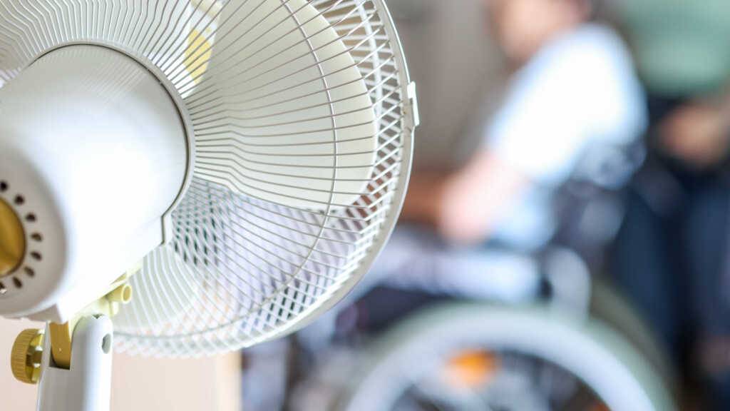 ARCHIV - Ein Ventilator steht in einem Aufenthaltsraum eines Seniorenheims, davor sitzt eine Seniorin in einem Rollstuhl. Foto: Christoph Reichwein/dpa