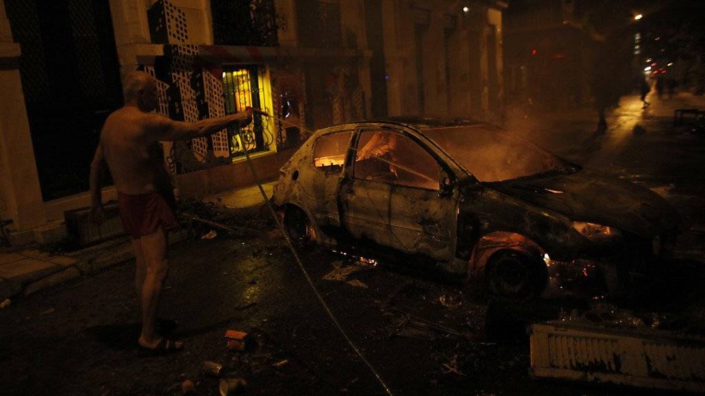 Mann beim Löschen eines zuvor bei Zusammenstössen in Brand gesetzten Autos im Athener Quartier Exarchia (Archiv)