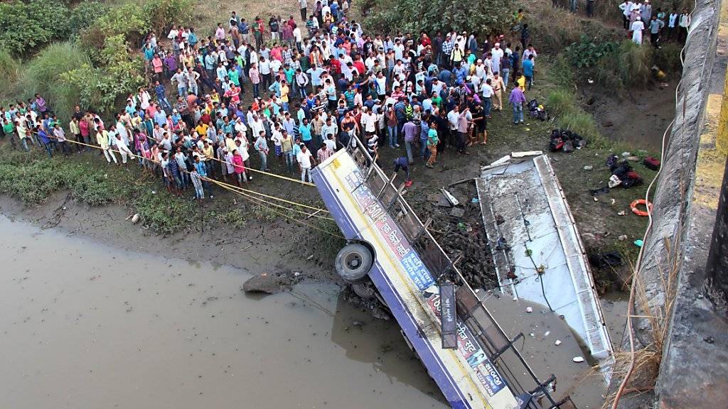 Schaulustige und Helfer versammeln sich um die Überreste des von einer Brücke gestürzten Busses.
