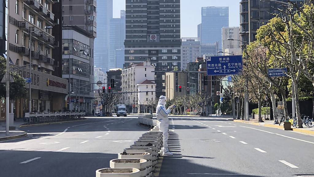Ein Mann in einem Schutzanzug steht auf einer fast menschenleeren Strasse in einem abgesperrten Gebiet im Westen von Shanghai.