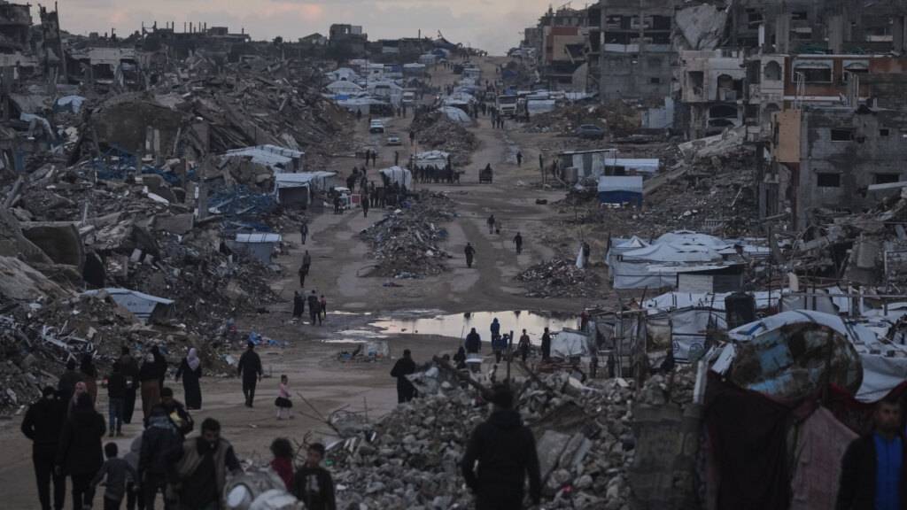 ARCHIV - Palästinenser gehen an zerstörten Gebäuden im nördlichen Gazastreifen vorbei. Foto: Jehad Alshrafi/AP/dpa/Archivbild