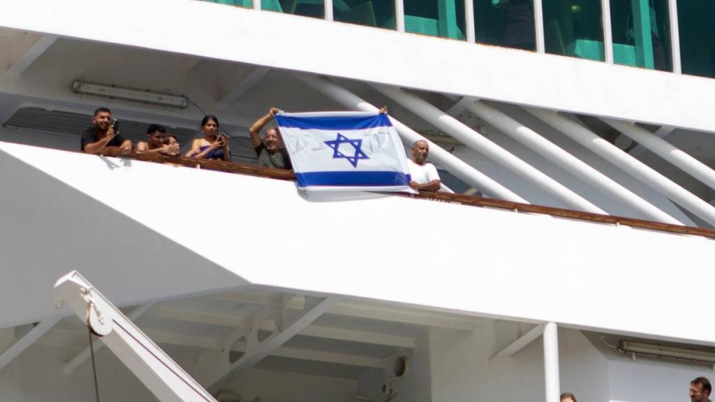 Zwei Männer halten eine israelische Flagge hoch, während ein Kreuzfahrtschiff mit israelischen Touristen auf der südöstlichen Ägäisinsel Rhodos, Griechenland, ablegt. Foto: Uncredited/InTime News/dpa