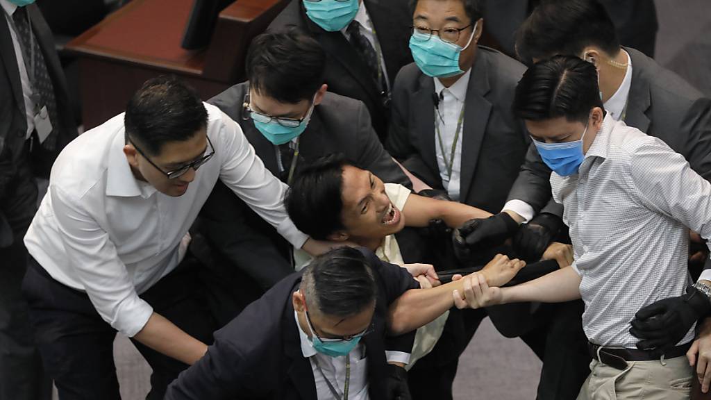 Eddie Chu Hoi-Dick (M), Mitglied des Legislativrates, wird von Sicherheitskräften abgeführt, nachdem es während einer Ausschusssitzung des Legislativrats zu Auseinandersetzungen zwischen den Teilnehmern kam. Foto: Vincent Yu/AP/dpa