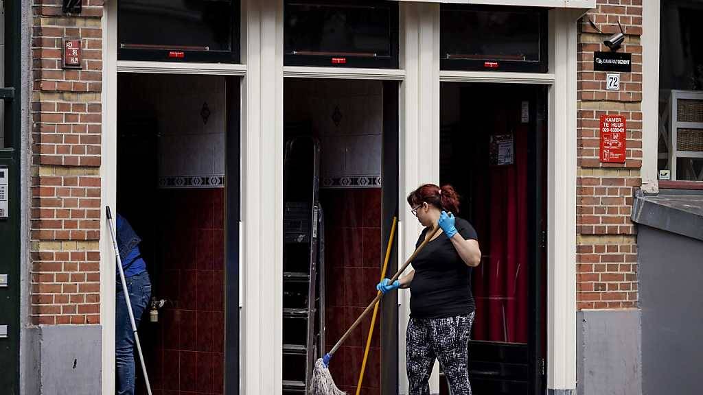 Eine Frau reinigt im Rotlichtviertel Wallen den Zugang zu Räumlichkeiten, die The Office 52 an Sexarbeiter vermietet. Ab 01.07.2020 dürfen nach einem Beschluss der Regierung alle Sexarbeiter im Land wieder uneingeschränkt ihrem Gewerbe nachgehen. Foto: «robin Van Lonkhuijsen»/ANP/dpa