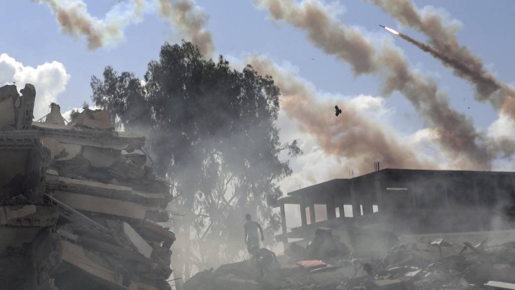ARCHIV - Raketen aus dem Gazastreifen werden über zerstörte Gebäude hinweg auf Israel abgefeuert. Foto: Mohammed Dahman/AP/dpa