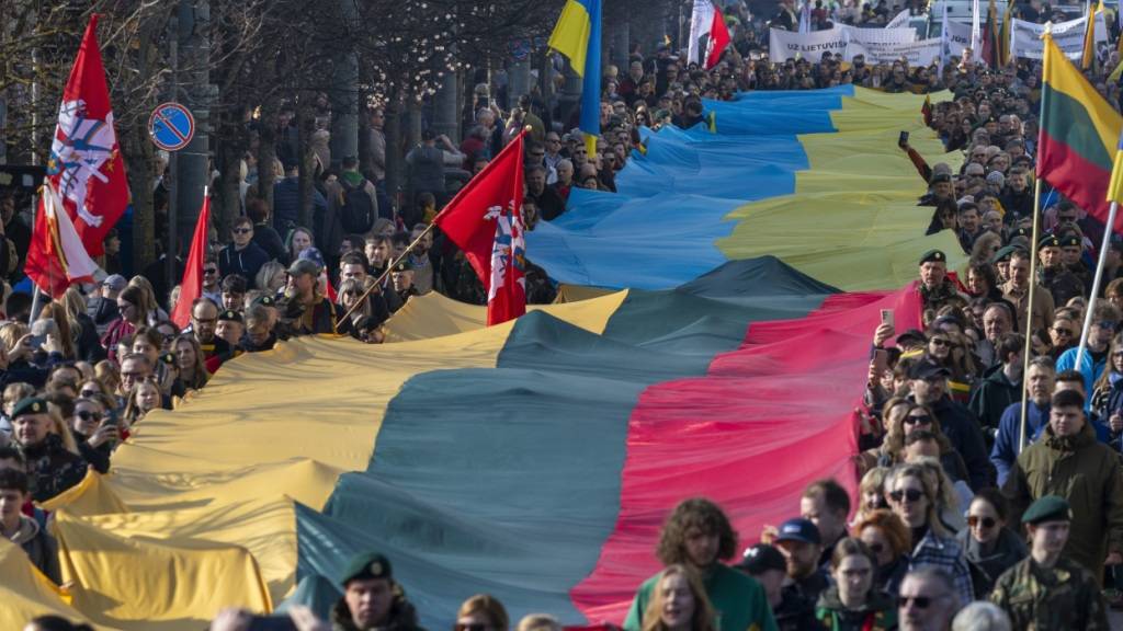 ARCHIV - Während einer Feier zum 35. Jahrestag der Unabhängigkeit Litauens von der Sowjetunion, tragen Menschen eine riesige ukrainische und eine litauische Fahne, um gegen den russischen Einmarsch in der Ukraine zu protestieren. Foto: Mindaugas Kulbis/AP/dpa