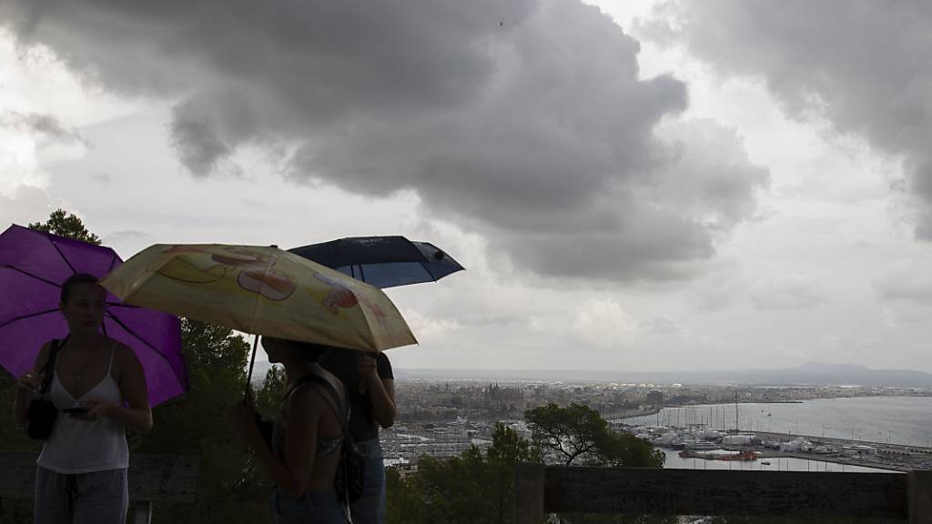 dpatopbilder - Passanten sind am Castell de Bellver auf Mallorca mit Regenschirmen unterwegs. Foto: Clara Margais/dpa