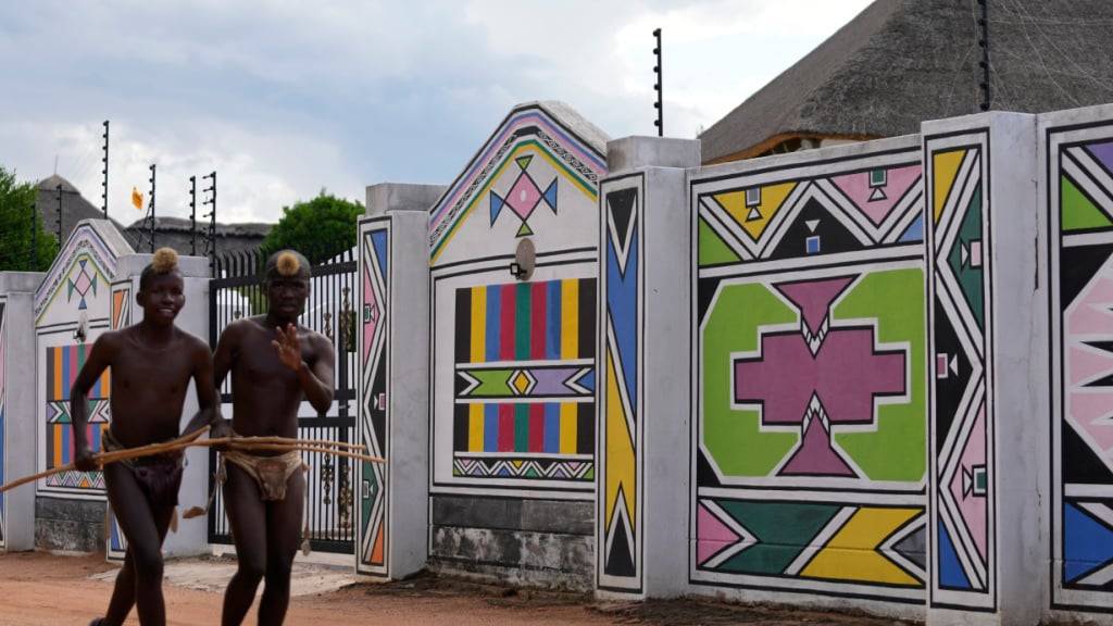 ARCHIV - Junge Männer vom Volk der Ndebele laufen am Haus von Esther Mahlangu, einer zeitgenössischen südafrikanischen Künstlerin, in KwaMhlanga in Mpumalanga, Südafrika, vorbei. Als Teil der Ndebele-Kultur durchlaufen Jungen einen traditionellen Initiationsprozess, bei dem ein Junge zum Mann wird. Foto: Themba Hadebe/AP/dpa