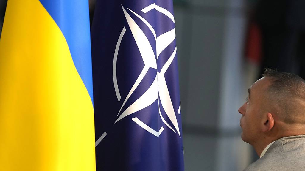 Symbolbild: Ein Mitglied des Protokolls richtet die NAato- und die ukrainische Flagge vor einer Pressekonferenz des ukrainischen Präsidenten Selenskyj und des Nato-Generalsekretärs Stoltenberg im Nato-Hauptquartier. Foto: Virginia Mayo/AP/dpa