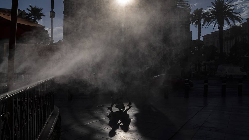 dpatopbilder - Menschen gehen in Las Vegas an Nebelmaschinen vorbei, die zur Abkühlung entlang des Las Vegas Strip eingesetzt werden. Las Vegas könnte an diesem Wochenende sein Temperatur-Allzeithoch erreichen, da für den Bundesstaat und große Teile der westlichen USA extreme Hitze vorhergesagt wird. Foto: John Locher/AP/dpa