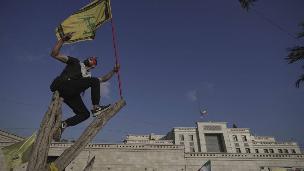 ARCHIV - Ein Hisbollah-Anhänger schwenkt eine Hisbollah-Fahne und macht ein Selfie, während er auf einem Baum vor der iranischen Botschaft in Beirut steht. Foto: Hassan Ammar/AP/dpa