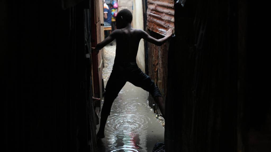 Ein Junge bewegt sich in einer vom Regen des Hurrikans «Melissa» überfluteten Gasse in einer Notunterkunft für Familien, die durch Bandengewalt vertrieben wurden. Foto: Odelyn Joseph/AP/dpa
