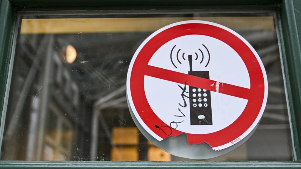 ARCHIV - Ein Schild mit einem durchgestrichenen Handysymbol weist in einer Schule auf das Handyverbot hin. Foto: Jens Kalaene/dpa/Symbolbild