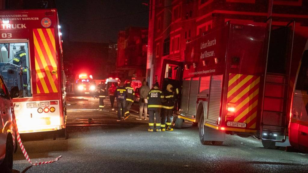 Feuerwehrleute stehen für Löscharbeiten auf einer Straße, nahe eines brennenden Gebäudes. Im Zentrum der Stadt sind bei einem Feuer in einem Gebäude mindestens 58 Menschen ums Leben gekommen. Foto: Uncredited/AP/dpa