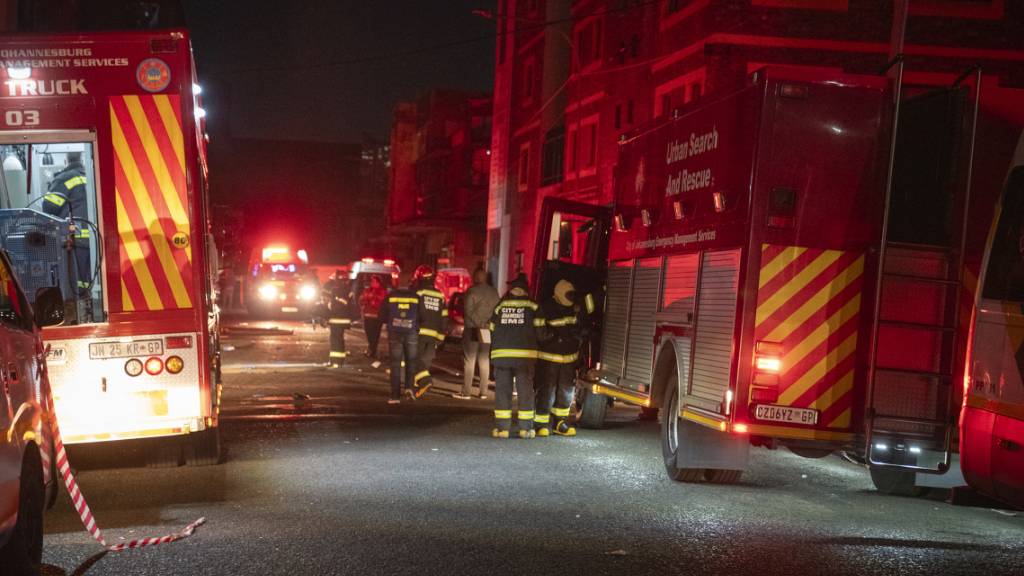 Feuerwehrleute stehen für Löscharbeiten auf einer Straße, nahe eines brennenden Gebäudes. Im Zentrum der Stadt sind bei einem Feuer in einem Gebäude mindestens 58 Menschen ums Leben gekommen. Foto: Uncredited/AP/dpa