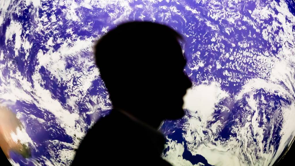 Ein Mann sitzt bei der UN-Klimakonferenz COP26 vor einem leuchtenden Globus. Foto: Christoph Soeder/dpa