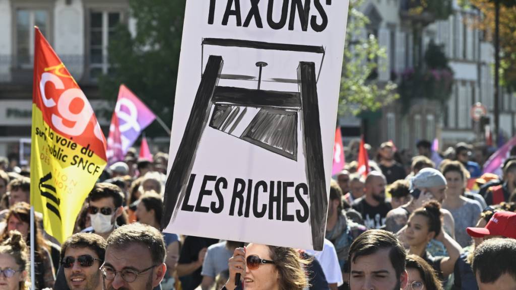 dpatopbilder - Ein Demonstrant hält ein Plakat mit der Aufschrift «Lasst uns die Reichen besteuern» während einer Kundgebung der Protestbewegung «Bloquons Tout» (Alles blockieren). Foto: Pascal Bastien/AP/dpa