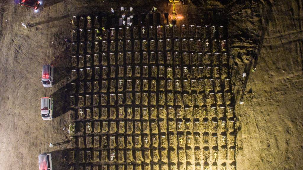 dpatopbilder - In Jakarta stehen Mitarbeiter (oben) in weißer Schutzkleidung um Gräber herum, während neben ihnen ein Bagger weitere Gräber aushebt. In Indonesien sind mehr als 69 000 Menschen in Verbindung mit Covid-19 gestorben. Foto: Wisnu Prasetyo/SOPA Images via ZUMA Wire/dpa
