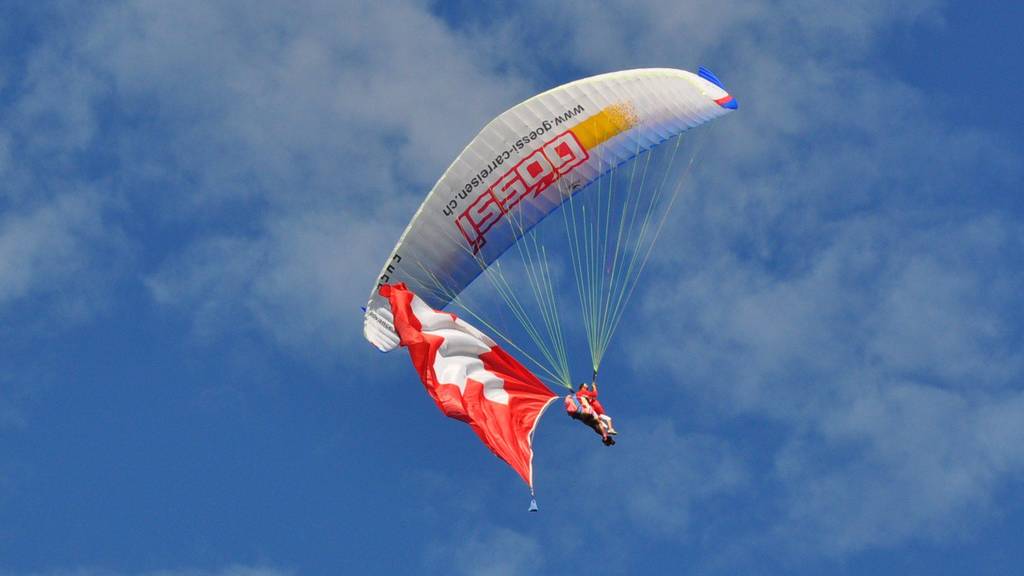 Gleitschirmpiloten fliegen mit Schweizer Fahne über Emmetten