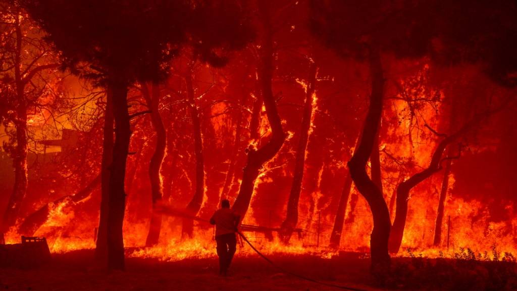 dpatopbilder - Ein Mann geht mit einem Löschschlauch auf die Flammen eines Waldbrandes auf der Ferieninsel Lesbos zu. Foto: Eurokinissi/Eurokinissi via ZUMA Press Wire/dpa