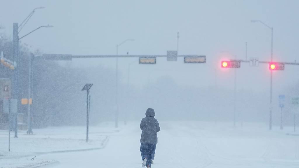 Ein Jogger läuft während eines Wintersturms über eine schneebedeckte Straße. Foto: Julio Cortez/AP/dpa