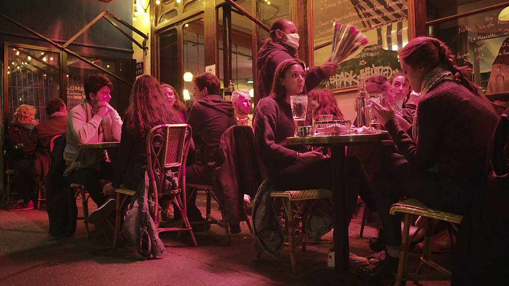 Menschen sitzen an Tischen auf einer Caféterrasse in Paris. Erneut gibt es Einschränkungen bei den Öffnungszeiten von Bars und Restaurants. Foto: Lewis Joly/AP/dpa