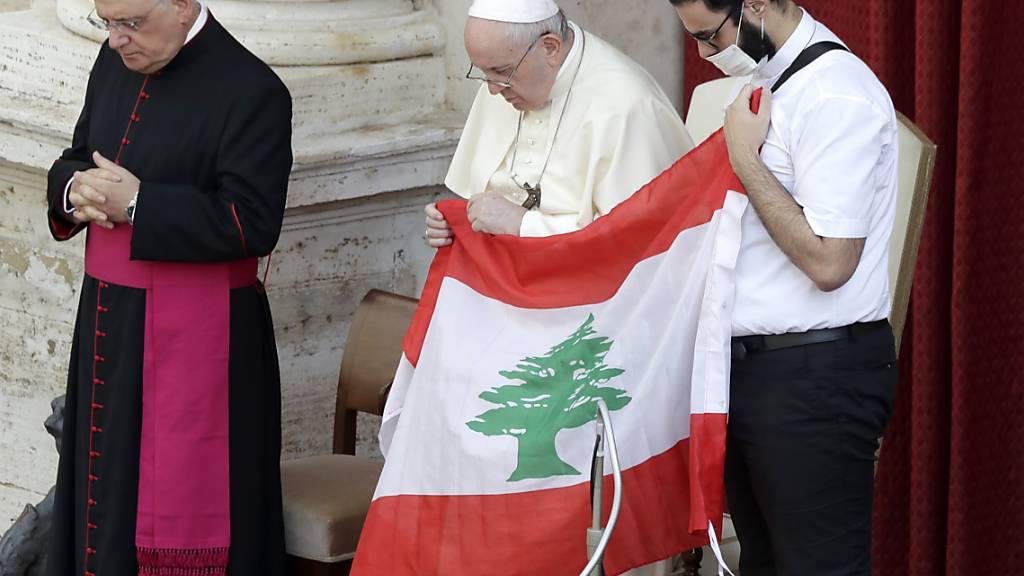 Papst Franziskus (M) hält bei seiner ersten Generalaudienz mit Gläubigen seit Ausbruch der Corona-Pandemie in Gedenken an die Opfer der Explosion die Flagge des Libanon. Foto: Andrew Medichini/AP/dpa