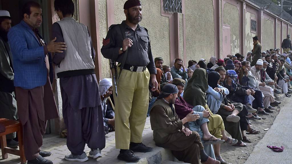 ARCHIV - Ein Polizist steht Wache, während afghanische Einwanderer vor dem afghanischen Konsulat warten, um Reisedokumente für die Rückkehr in ihr Heimatland zu erhalten. Foto: Arshad Butt/AP/dpa