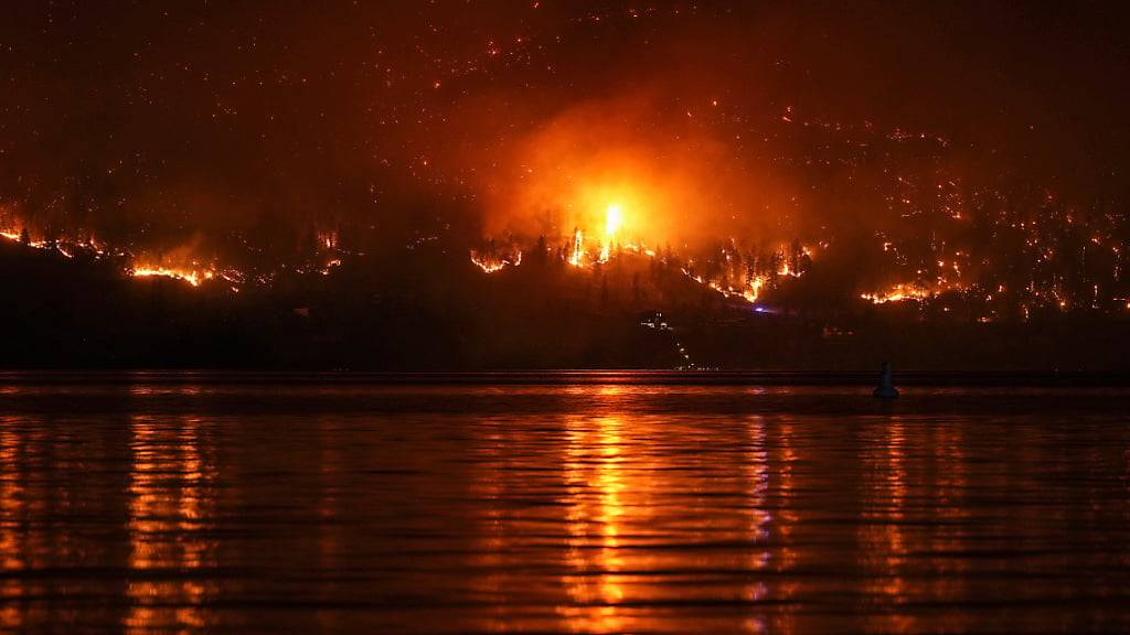 Ein Waldbrand am McDougall Creek an einem Berghang oberhalb eines Hauses am Seeufer. Foto: Darryl Dyck/The Canadian Press/AP/dpa