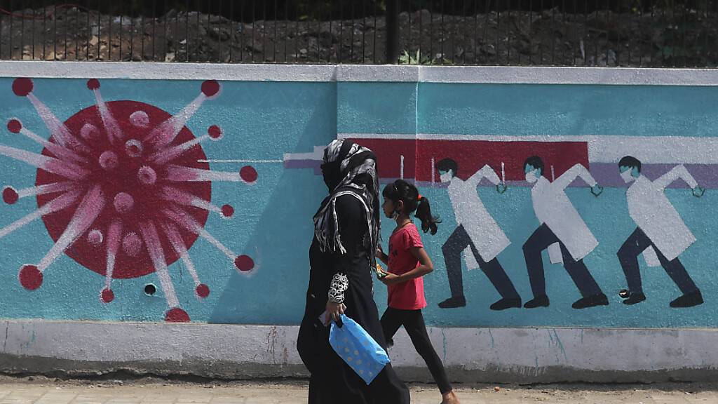 Eine Frau geht zusammen mit einem Mädchen an einem Graffiti vorbei, das das Coronavirus darstellt. Foto: Rafiq Maqbool/AP/dpa