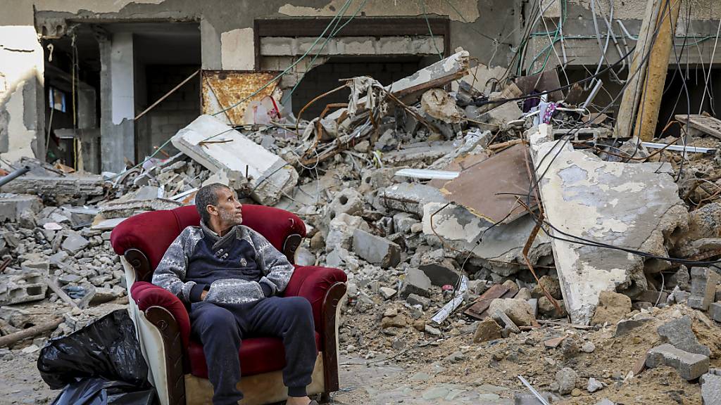 Ein palästinensischer Mann sitzt in einem Sessel vor einem zerstörten Gebäude in Gaza-Stadt. Foto: Mohammed Hajjar/AP/dpa