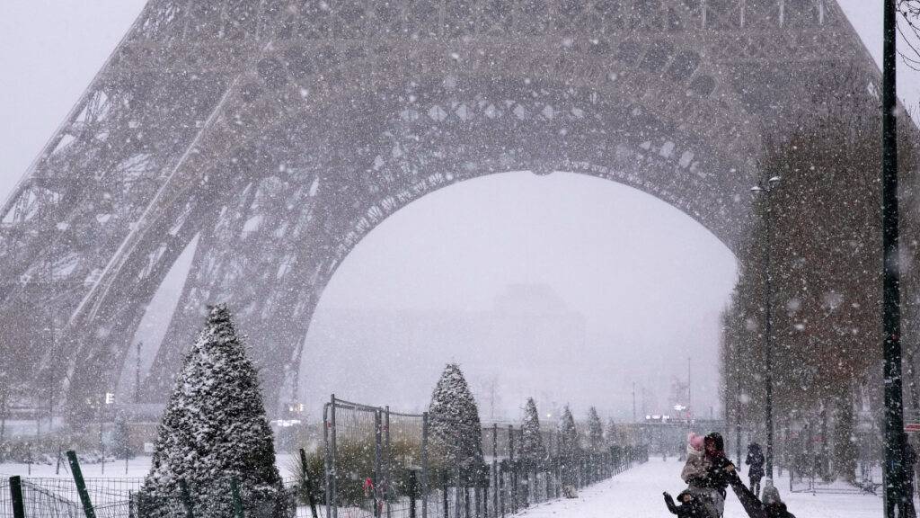dpatopbilder - Menschen spazieren bei Schneefall in der Nähe des Eiffelturms. Foto: Christophe Ena/AP/dpa