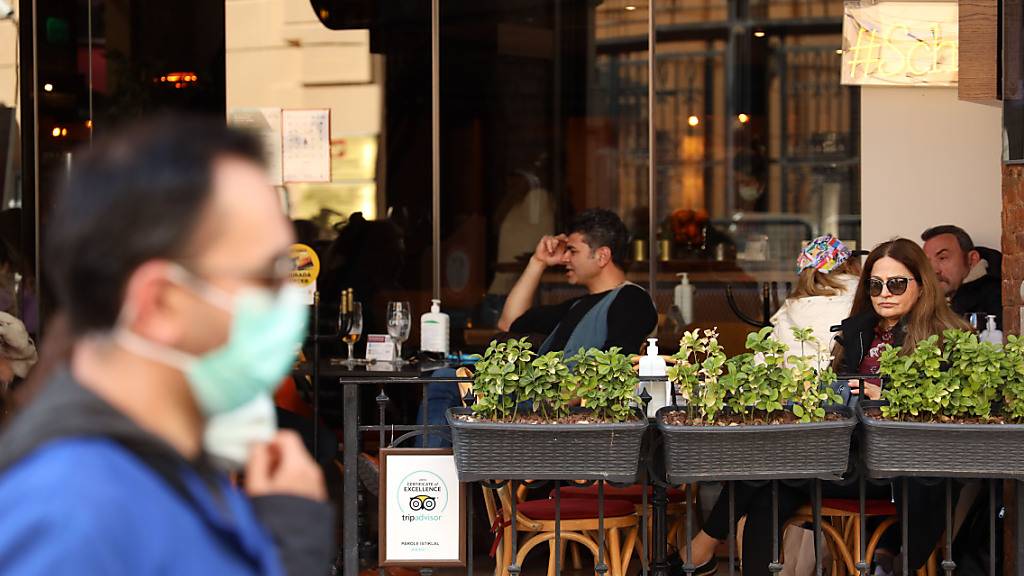 Ein Mann mit Mund-Nasen-Schutz läuft an einem Café in Istanbul vorbei, in dem einige Menschen sitzen. Foto: Shady Al-Assar/APA Images via ZUMA Wire/dpa