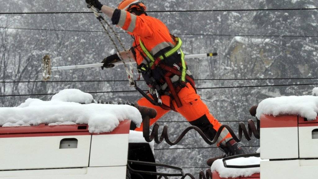 Ein Bahnarbeiter kontrolliert mit einem Schneebesen in der Hand eine Fahrleitung. Schneebedingte Fahrleitungsstörungen sind Standard, wenn es stark schneit - ein Eisblock, der wie im Val-de-Travers einen Zug stoppt, nicht. (Archiv)