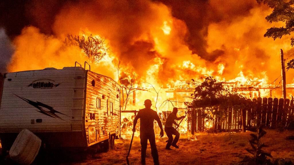 dpatopbilder - Anwohner arbeiten daran, ein Übergreifen der Flammen von einem brennenden Haus auf ein Nachbarhaus zu verhindern, während das 6-5-Feuer in der Gemeinde Chinese Camp in Tuolumne County brennt. Foto: Noah Berger/AP/dpa