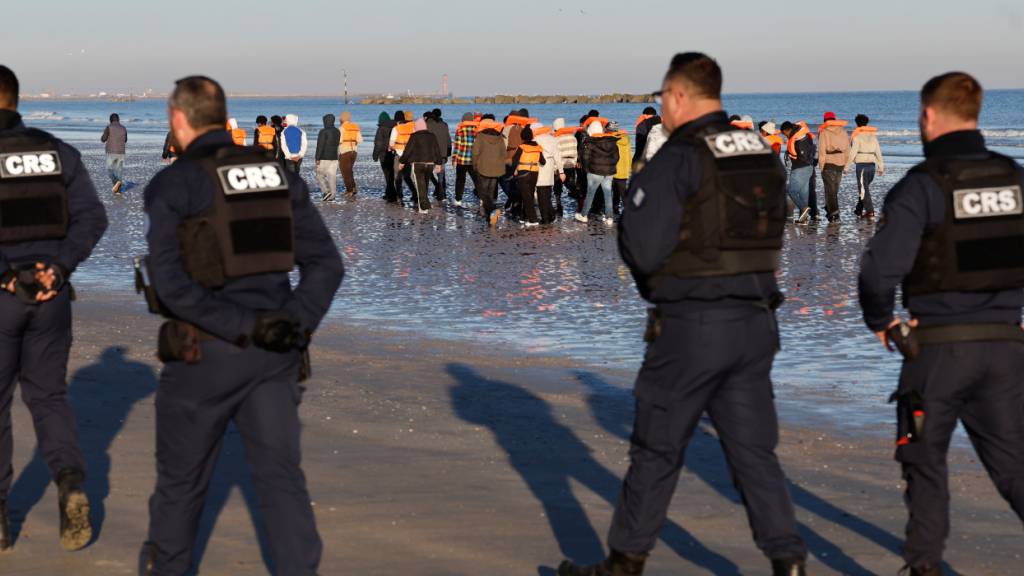Polizisten gehen in Malo-les-Bains an Migranten vorbei, die versuchen, Großbritannien zu erreichen (Archivbild). Foto: Jean-Francois Badias/AP/dpa