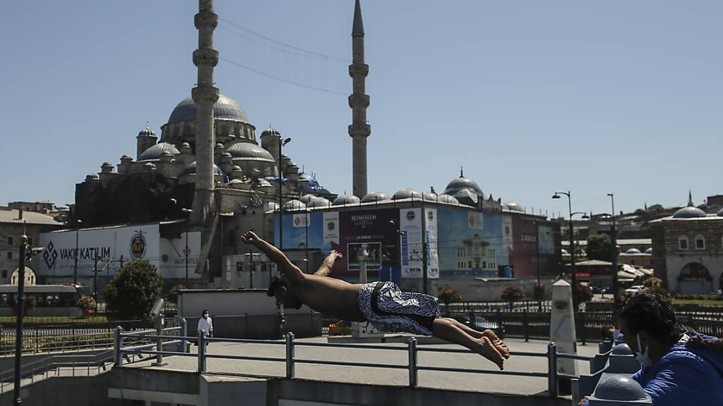 Vor dem Hintergrund der historischen Neuen Moschee springt ein Jugendlicher von der Galata Brücke in den Bosporus. Foto: Emrah Gurel/AP/dpa