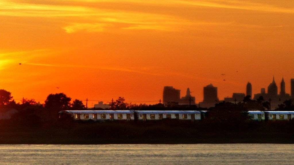 Ein Zug durchquert bei Sonnenuntergang die New Yorker Jamaica Bay. Im Hintergrund ragen die Wolkenkratzer von Manhattan in den Abendhimmel. New Yorks Bürgermeister Bill de Blasio will mit einer unorthodoxen Austernzucht die Wasserqualität des Feuchtgebiets verbessern. (Archiv)