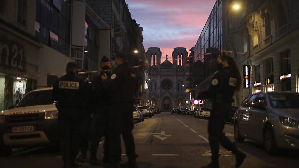 Polizisten gehen unter einem Absperrband vor der Kirche Notre Dame nach einem Messerangriff durch. Foto: Daniel Cole/AP/dpa