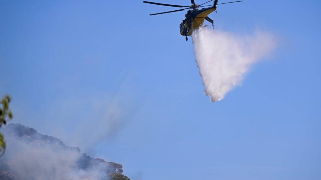 dpatopbilder - Ein Löschhubschrauber wirft nach einem Waldbrand im Dorf südöstlich von Athen Wasser auf ein wieder aufflammendes Feuer. Foto: Michael Varaklas/AP/dpa