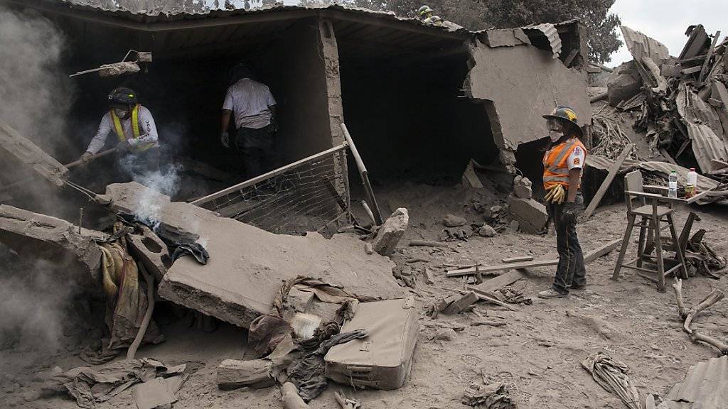 Feuerwehrleute suchen in mit Asche zugedeckten Trümmern nach Opfern des Vulkanausbruchs in der guatemaltekischen Ortschaft Escuintla.